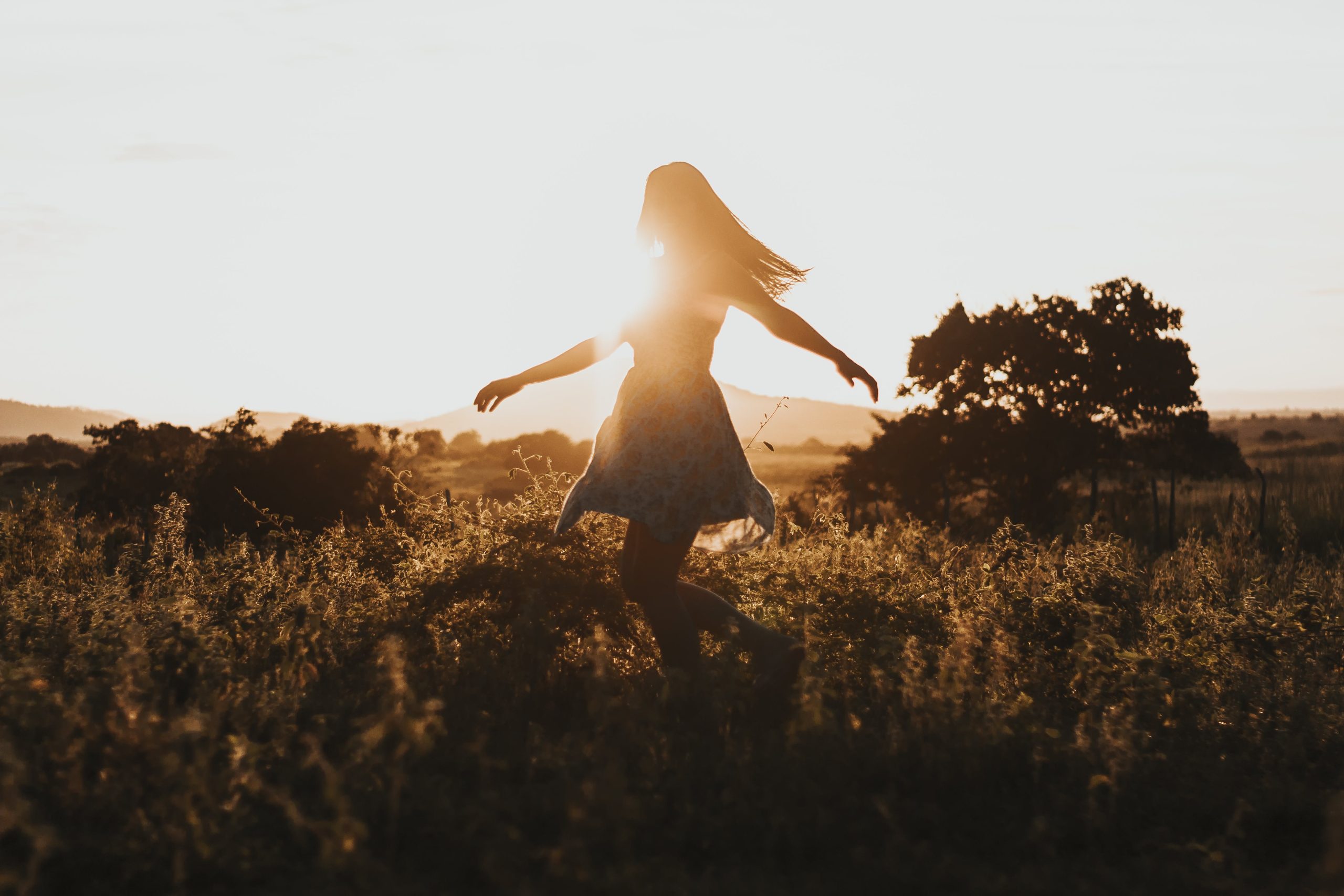 silhouette of woman dancing in a field during sunset